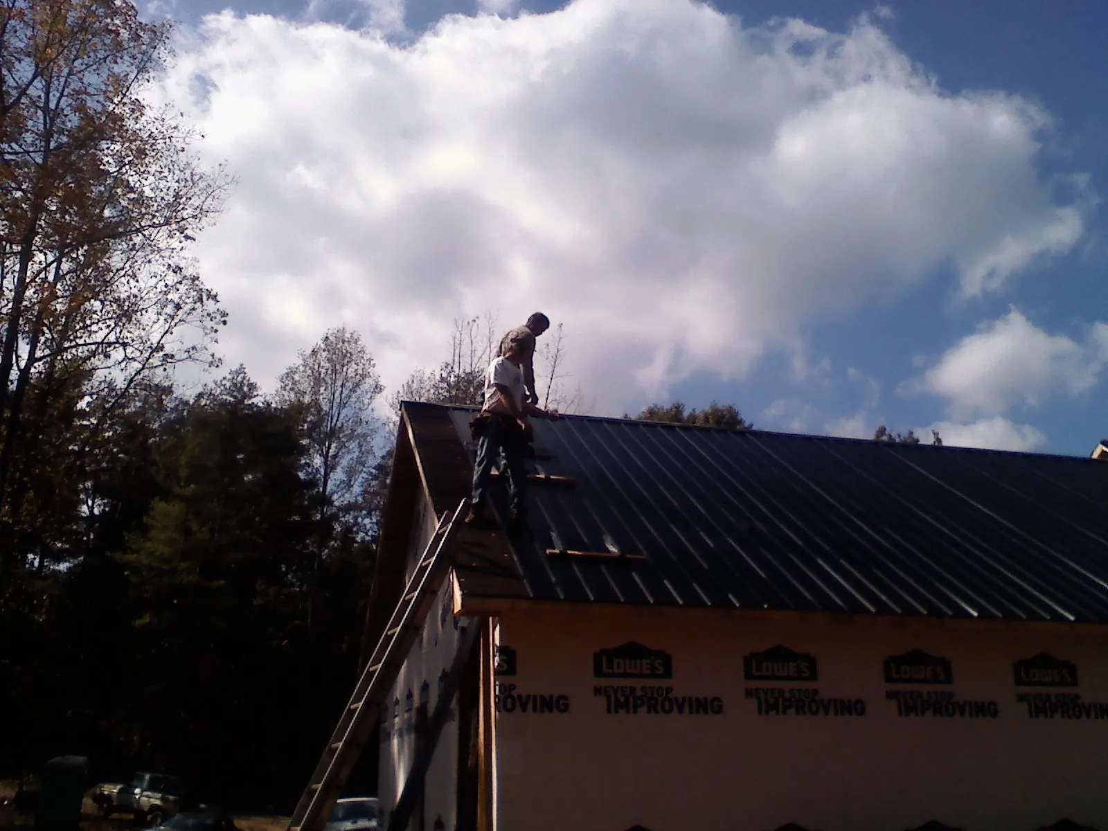 Roofer fastening dark metal panels high against a cloudy sky, from a Roof Inspection job in South Lake Tahoe